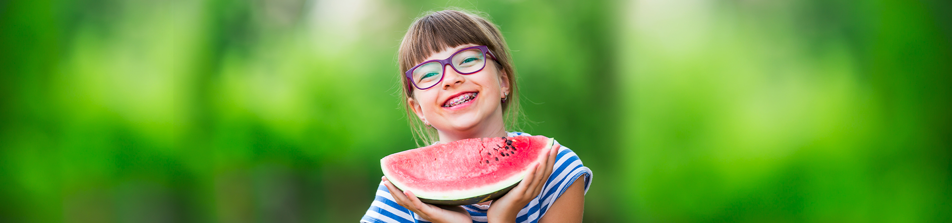 A cheerful child wearing braces poses in a dental office, highlighting her smile with orthodontic tools visible in the background at New Smile Dentistry.